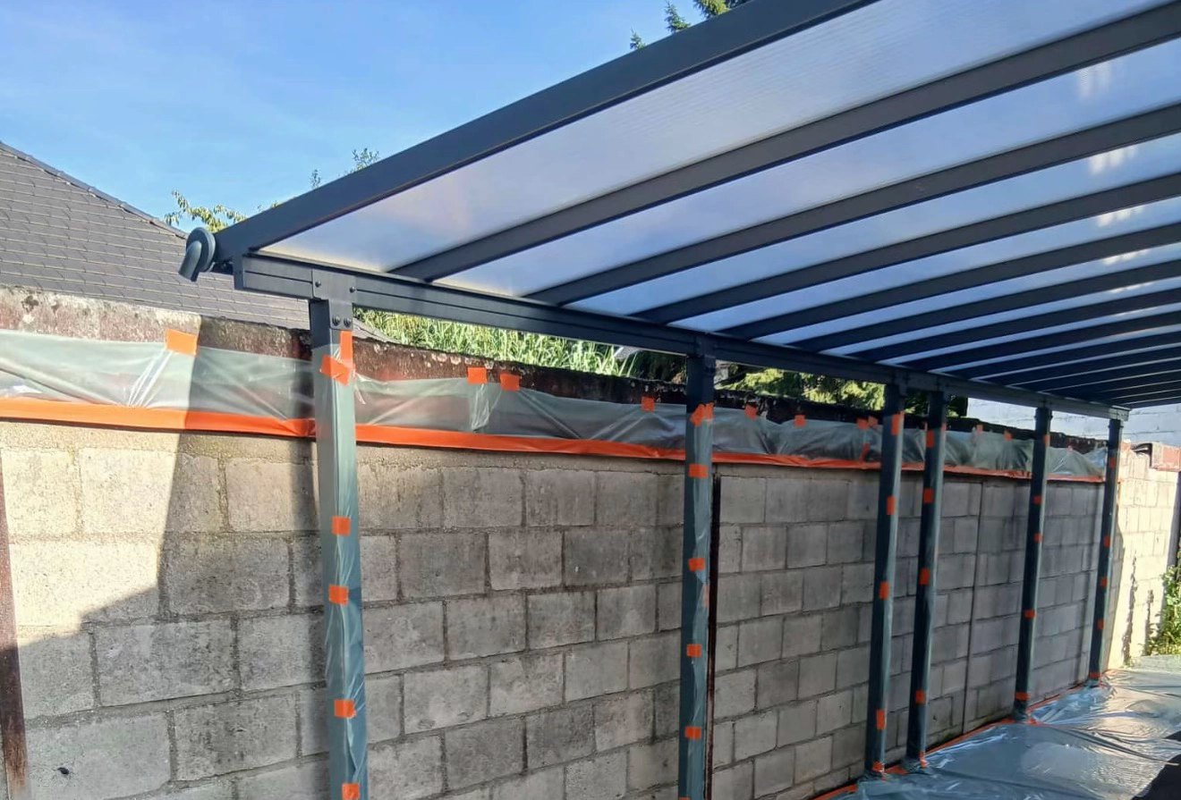 Avant : mur en blocs béton nu, poteaux du carport et sol protégés par film et adhésif